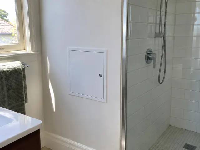 Bathroom wall with small access panel beside a tiled shower and window in Mascot
